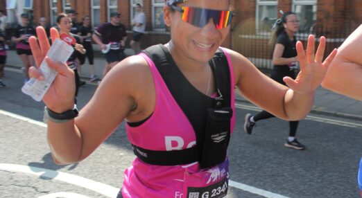 Runner in Refuge vest and sunglasses waving with both hands as they go