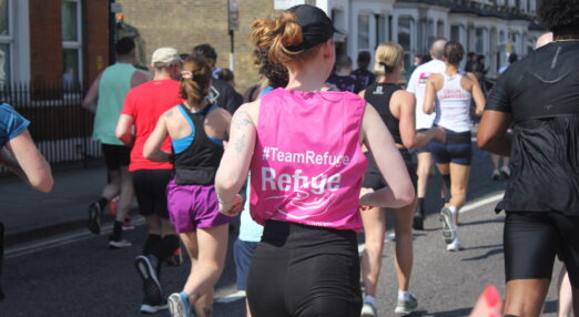 Photograph of a young, white woman with her back to the camera, running with a Refuge branded vest and a navy blue cap